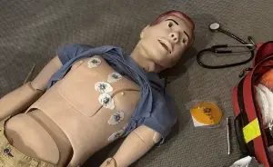 Eine medizinische Trainingspuppe liegt auf dem Boden, auf deren Brustkorb mehrere EKG-Elektroden für eine Herzrhythmus-Überwachung angebracht sind.